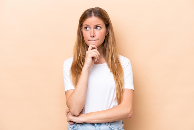 Jeune femme caucasienne isolée sur fond beige ayant des doutes et pensant