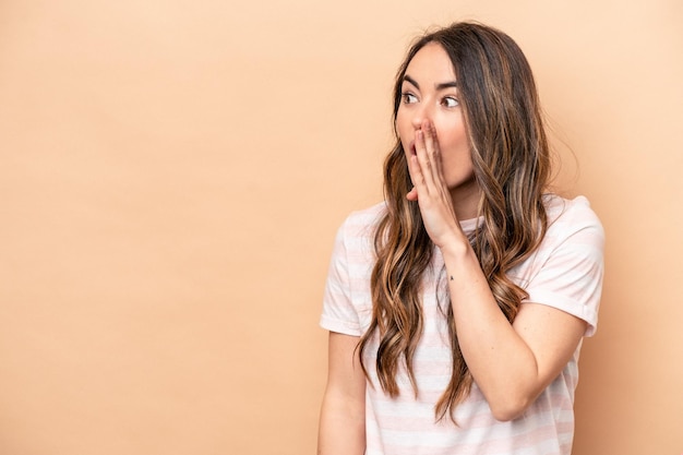 Jeune femme caucasienne isolée sur fond beige choquée à cause de quelque chose qu'elle a vu