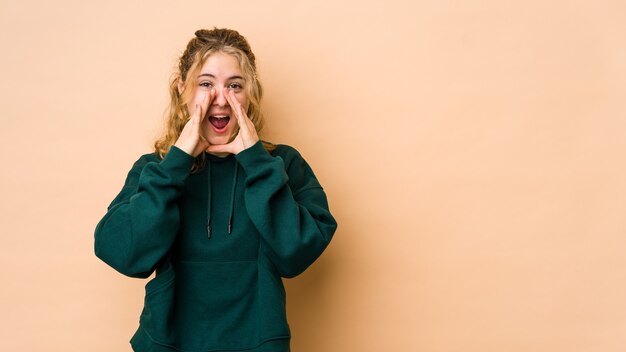 Jeune femme caucasienne isolée sur fond beige criant excité à l'avant.