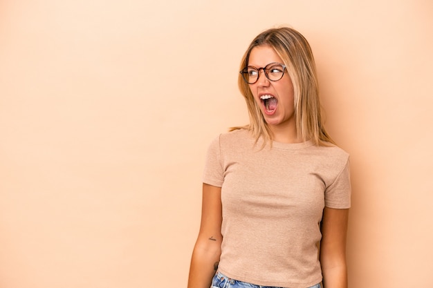 Jeune femme caucasienne isolée sur fond beige criant très en colère, concept de rage, frustré.