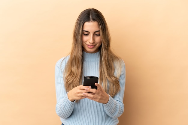 Jeune femme caucasienne isolée sur fond beige, envoyer un message avec le mobile