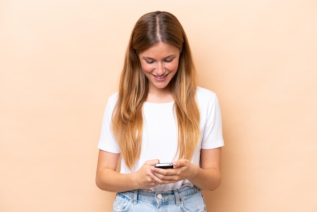 Jeune femme caucasienne isolée sur fond beige, envoyer un message avec le mobile