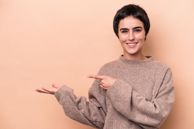 Jeune femme caucasienne isolée sur fond beige excitée tenant un espace de copie sur la paume.