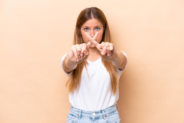 Jeune femme caucasienne isolée sur fond beige faisant un geste d'arrêt avec sa main pour arrêter un acte