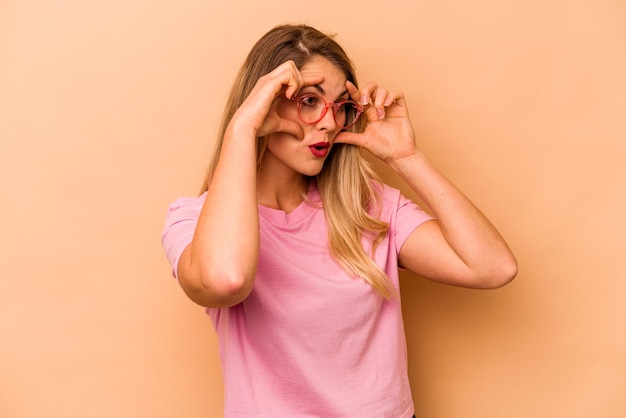 Jeune femme caucasienne isolée sur fond beige en gardant les yeux ouverts pour trouver une opportunité de succès