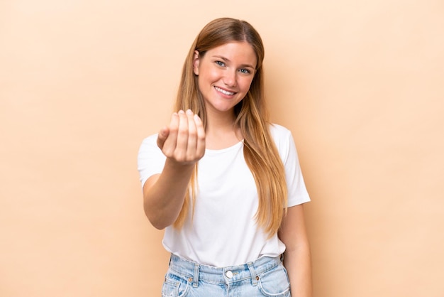 Jeune femme caucasienne isolée sur fond beige invitant à venir avec la main Heureux que vous soyez venu