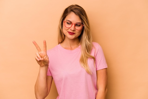 Jeune femme caucasienne isolée sur fond beige joyeuse et insouciante montrant un symbole de paix avec les doigts