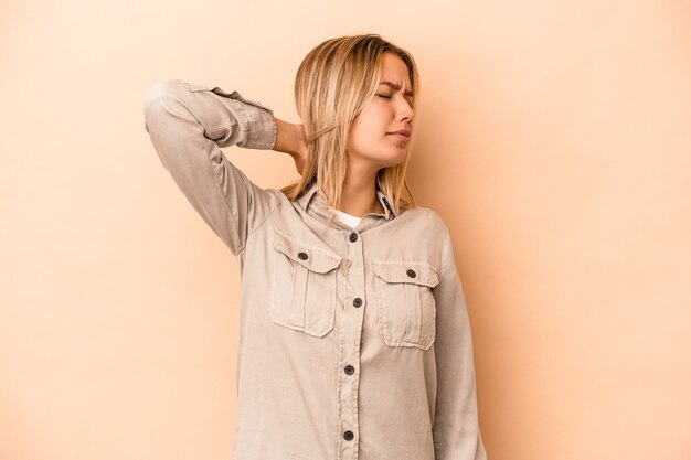 Jeune femme caucasienne isolée sur fond beige massant le coude, souffrant après un mauvais mouvement.