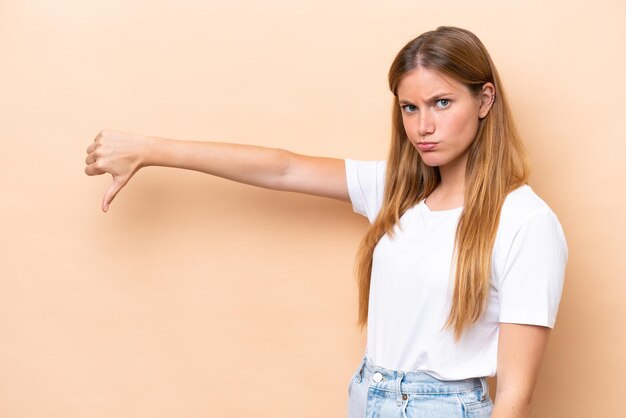 Jeune femme caucasienne isolée sur fond beige montrant le pouce vers le bas avec une expression négative