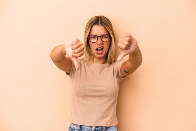 Jeune femme caucasienne isolée sur fond beige montrant le pouce vers le bas et exprimant son aversion.