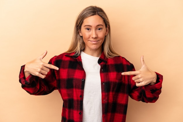 Photo jeune femme caucasienne isolée sur fond beige personne pointant à la main vers un espace de copie de chemise, fière et confiante