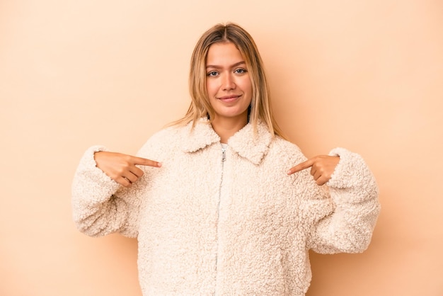 Jeune femme caucasienne isolée sur fond beige personne pointant à la main vers un espace de copie de chemise, fière et confiante