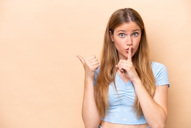 Jeune femme caucasienne isolée sur fond beige pointant vers le côté et faisant un geste de silence