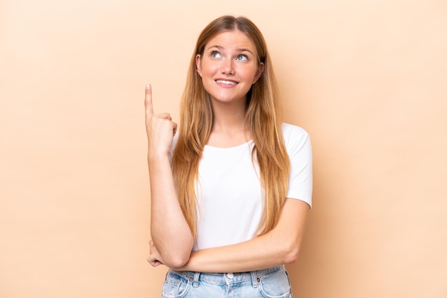 Jeune femme caucasienne isolée sur fond beige pointant vers le haut une excellente idée