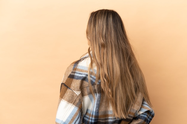 Jeune femme caucasienne isolée sur fond beige en position arrière et regardant en arrière