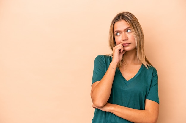 Jeune femme caucasienne isolée sur fond beige qui se sent triste et pensive, regardant l'espace de copie.