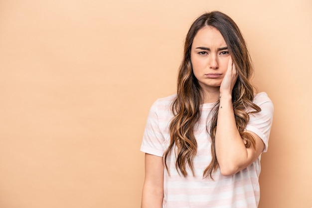 Jeune femme caucasienne isolée sur fond beige qui se sent triste et pensive en regardant l'espace de copie