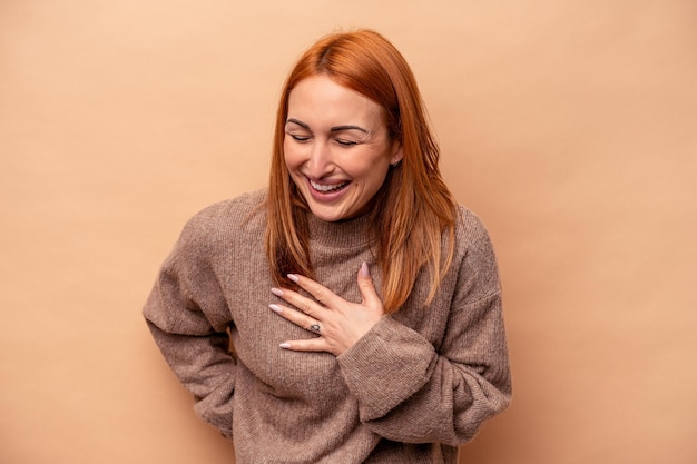 Jeune femme caucasienne isolée sur fond beige en riant en gardant les mains sur le cœur, concept de bonheur.