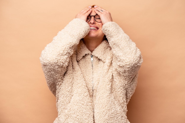 Jeune femme caucasienne isolée sur fond beige rit joyeusement en gardant les mains sur la tête. Notion de bonheur.