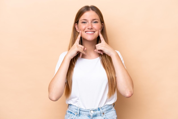 Jeune femme caucasienne isolée sur fond beige souriant avec une expression heureuse et agréable