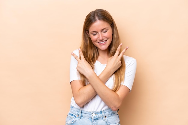 Jeune femme caucasienne isolée sur fond beige souriant et montrant le signe de la victoire