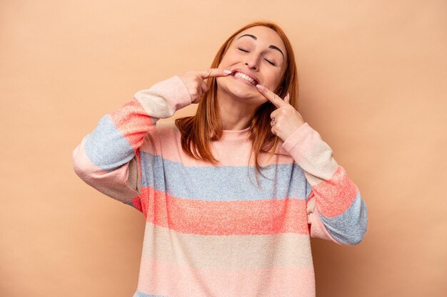 Jeune femme caucasienne isolée sur fond beige sourit pointant du doigt la bouche