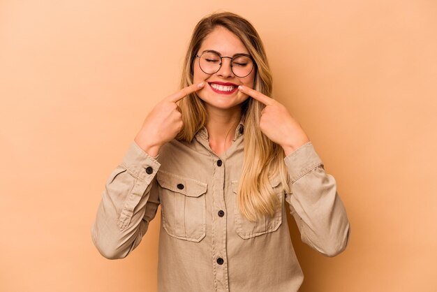 Jeune femme caucasienne isolée sur fond beige sourit pointant du doigt la bouche