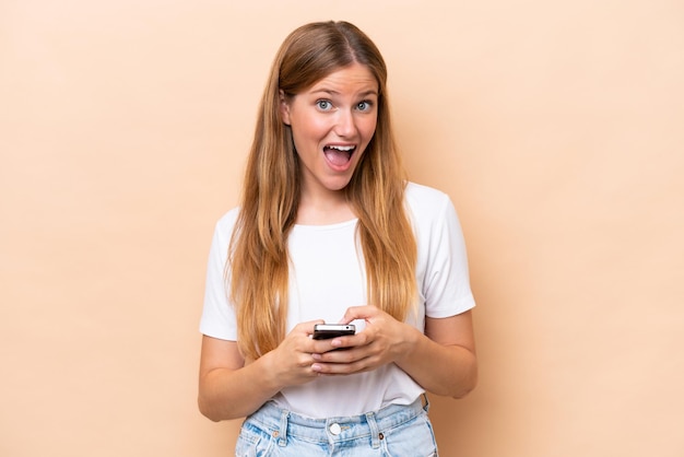 Jeune femme caucasienne isolée sur fond beige surpris et envoyant un message