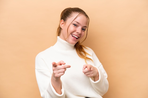 Jeune femme caucasienne isolée sur fond beige surpris et pointant vers l'avant