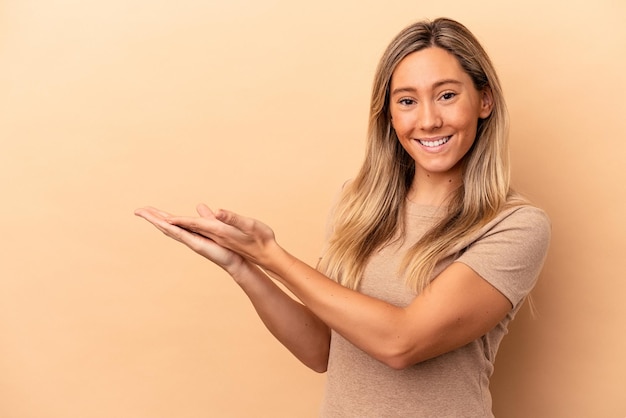 Jeune femme caucasienne isolée sur fond beige tenant un espace de copie sur une paume.