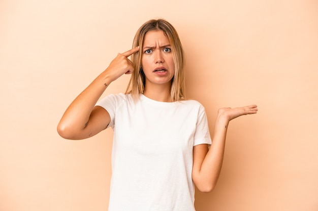 Jeune femme caucasienne isolée sur fond beige tenant et montrant un produit à portée de main.