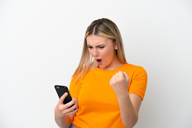 Jeune femme caucasienne isolée sur fond blanc à l'aide d'un téléphone portable et faisant le geste de la victoire