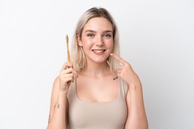 Jeune femme caucasienne isolée sur fond blanc avec une brosse à dents et une expression heureuse