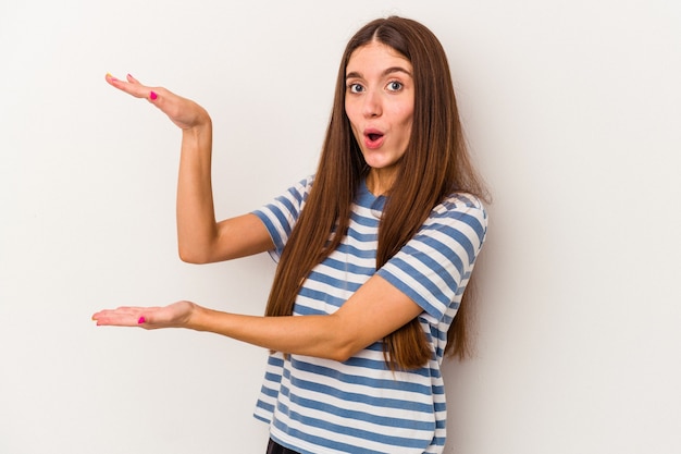 Jeune femme caucasienne isolée sur fond blanc choquée et étonnée tenant un espace de copie entre les mains.