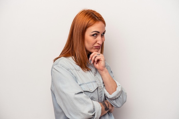 Jeune femme caucasienne isolée sur fond blanc contemplant, planifiant une stratégie, réfléchissant à la voie d'une entreprise.