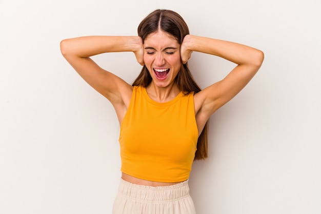 Jeune femme caucasienne isolée sur fond blanc couvrant les oreilles avec les mains en essayant de ne pas entendre un son trop fort.