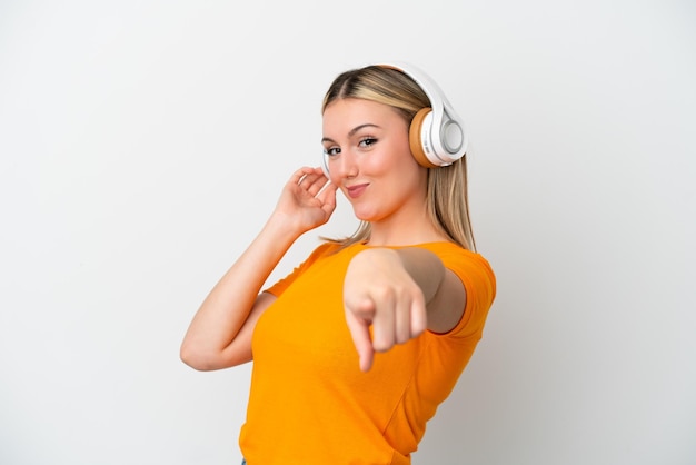 Jeune femme caucasienne isolée sur fond blanc, écoutant de la musique et pointant vers l'avant