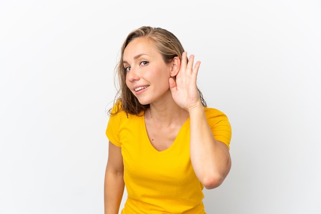 Photo jeune femme caucasienne isolée sur fond blanc écoutant quelque chose en mettant la main sur l'oreille