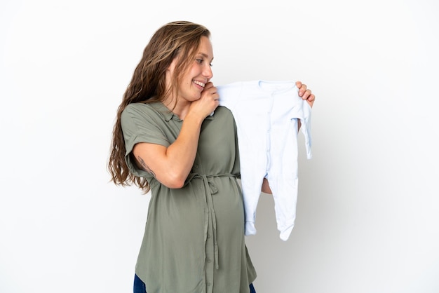 Jeune femme caucasienne isolée sur fond blanc enceinte et tenant des vêtements de bébé