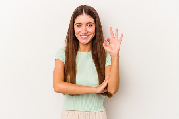 Jeune femme caucasienne isolée sur fond blanc fait un clin d'œil et tient un geste correct avec la main.