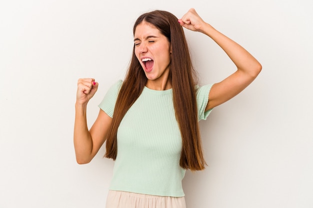 Jeune femme caucasienne isolée sur fond blanc levant le poing après une victoire, concept gagnant.