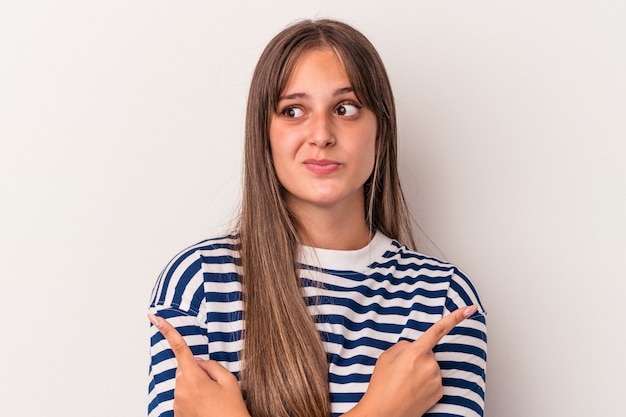 Jeune femme caucasienne isolée sur fond blanc pointe sur le côté, essaie de choisir entre deux options.