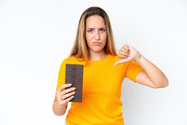 Jeune femme caucasienne isolée sur fond blanc prenant une tablette de chocolat faisant un mauvais signal