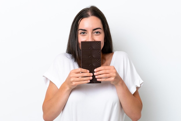 Jeune femme caucasienne isolée sur fond blanc prenant une tablette de chocolat et heureux