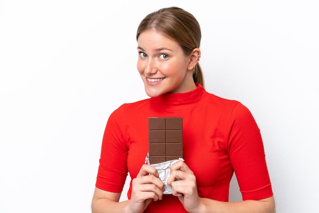 Jeune femme caucasienne isolée sur fond blanc prenant une tablette de chocolat et heureux