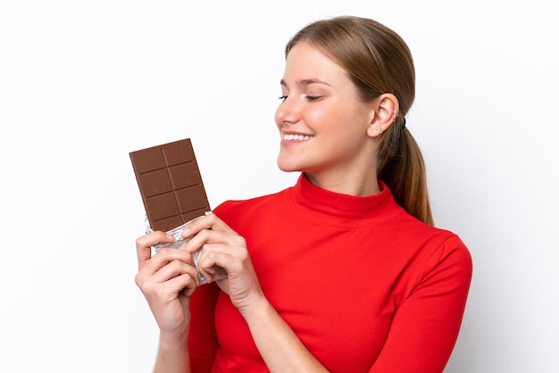 Jeune femme caucasienne isolée sur fond blanc prenant une tablette de chocolat et heureux