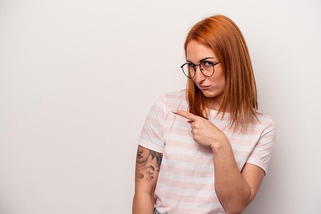 Jeune femme caucasienne isolée sur fond blanc souriant et pointant de côté montrant quelque chose à l'espace vide