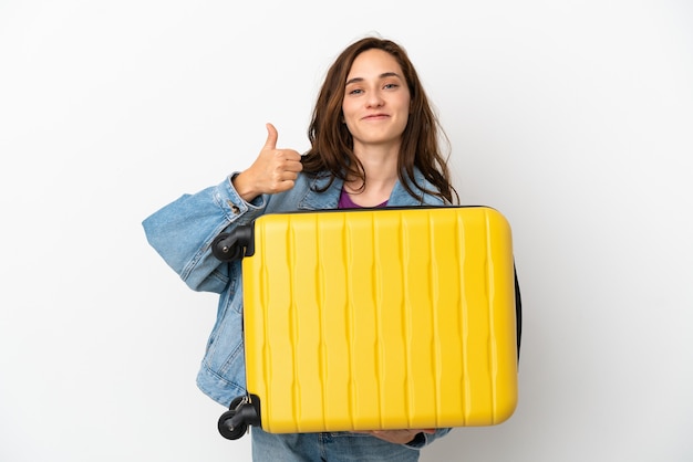 Jeune femme caucasienne isolée sur fond blanc en vacances avec valise de voyage et avec le pouce vers le haut