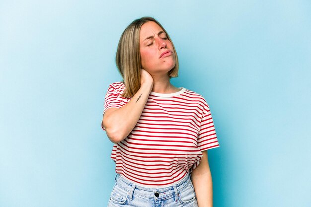 Jeune femme caucasienne isolée sur fond bleu ayant une douleur au cou due au stress massant et la touchant avec la main