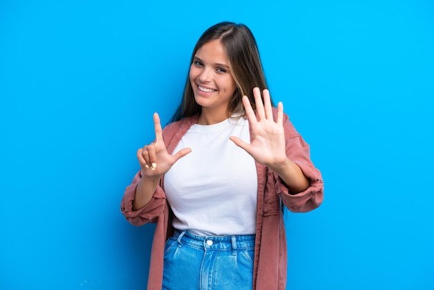 Jeune femme caucasienne isolée sur fond bleu comptant sept avec les doigts